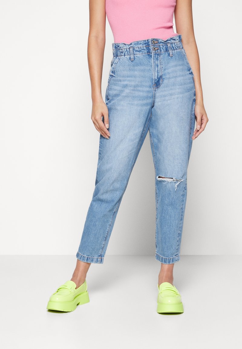 Korkeavyötäröiset, vaaleansiniset farkut, joissa on kulunut polvi, suora lahje, yhdistetty kirkkaan vihreisiin platform-kenkiin.