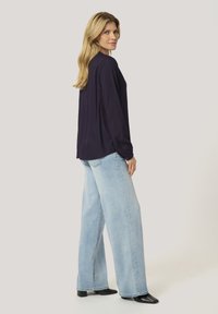 Navy long-sleeve blouse paired with light blue wide-leg jeans. The blouse features a relaxed fit and buttoned cuffs, while jeans are unembellished.