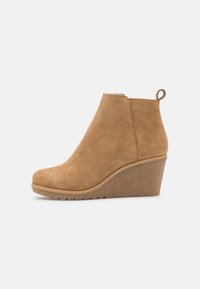 Stivaletto alla caviglia in suede beige con tacco a zeppa arrotondato, zeppa texturizzata e dettagli cuciti lungo la suola. Dotato di una linguetta per una facile calzata.