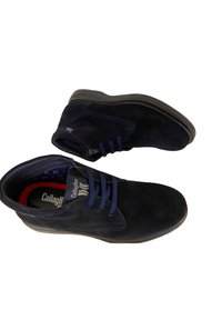 Chaussures en suède bleu marine à design bas et lacets bleus, avec des semelles extérieures en caoutchouc brun contrastant. Présente un logo sur la semelle intérieure.