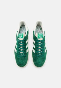 Green suede sneakers with white three-stripe accents, lace-up design, and a patterned insole featuring the Adidas logo.