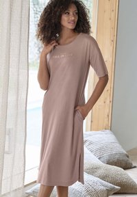 Light pink, short-sleeve dress in soft fabric with side pockets and a hem slit. Text "FALL IN LOVE" in light gold on the front.