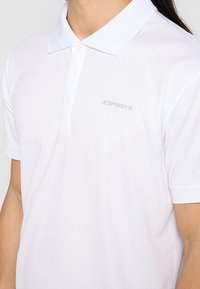 Camiseta polo blanca fabricada en una tela suave, con un collar clásico, tapeta de tres botones y un logo sutil en el pecho.