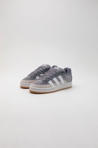 Sneaker in suede grigio con strisce bianche e suole in gomma. Presenta lacci rotondi, punta perforata e colletto imbottito per un supporto maggiore.