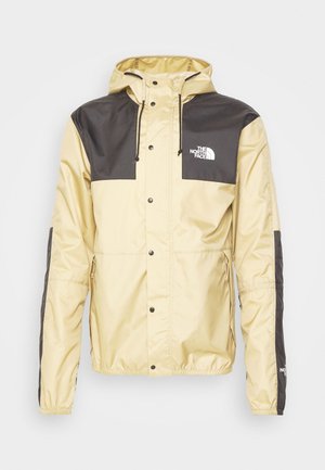 Chaqueta resistente al agua en beige y negro. Cuenta con capucha, botones a presión y puños elásticos. Logo de la marca en el bolsillo del pecho. Material ligero.