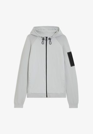 Hoodie cinza claro com fecho zip e mangas de malha, cordões ajustáveis no capuz, bolsos laterais e um bolso com fecho zip preto na manga esquerda.