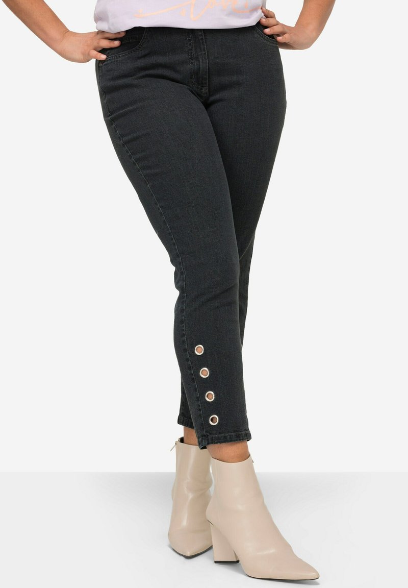 Zwarte denim jeans met een slim fit, voorzien van knoopaccenten aan de zoom en gecombineerd met beige blokhak enkellaarzen.