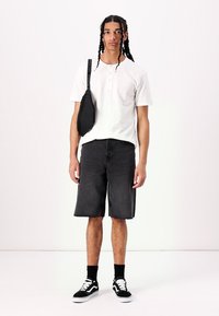 White short-sleeved henley shirt, black denim shorts, black crossbody bag, black socks, black and white sneakers, braided hair.
