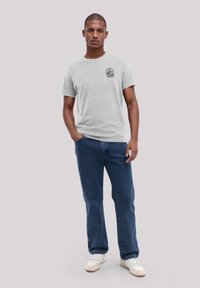 Grijze T-shirt met korte mouwen en een ronde halslijn, voorzien van een grafische print op de linkerborst, gecombineerd met blauwe spijkerbroeken en witte sneakers.