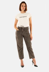 Wit T-shirt met de tekst "Saint Honoré", gecombineerd met bruin corduroy broek met textuur en zwarte hoge hakken. Eenvoudige, casual outfit.