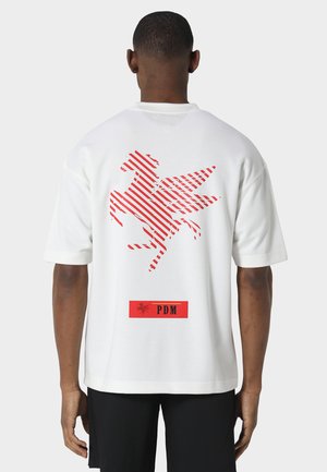 Mann trägt weißes T-Shirt mit rot gestreiftem Pegasus-Logo und rotem "PDM"-Label auf dem Rücken, kombiniert mit schwarzen Shorts.