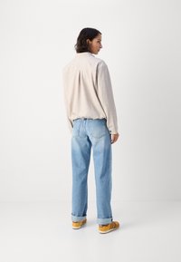 Camicia button-up beige chiara, jeans larghi blu chiaro e sneakers gialle. L'outfit presenta una vestibilità rilassata con i polsini arrotolati.