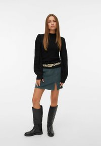Un pull noir avec des manches bouffantes, associé à une mini-jupe teal avec une fente sur le devant. Accentué par une ceinture à rayures zèbre et des bottes noires jusqu'aux genoux.