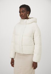 Giacca a vento in morbido tessuto bianco, con cappuccio, zip frontale e sezioni oversize trapuntate. Texture liscia con polsini elasticizzati.