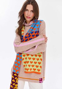 Pletený sveter v béžovej farbe s ružovými pruhmi, doplnený viacfarebnou šatkou s motívom sŕdc v oranžovej, modrej a zelenej farbe. Textúrovaný povrch.