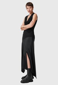 Top nero a costine abbinato a una gonna maxi nera fluida con uno spacco alto. La modella indossa stivaletti neri alla caviglia.