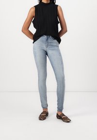 Schwarzes ärmelloses Oberteil mit vertikalen Falten, hellblaue Skinny-Jeans mit distressed Details und braune Ballerinas mit Leopardenmuster und schwarzen Riemen.