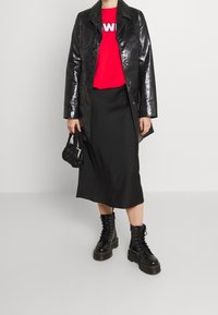 Błyszczący czarny skórzany płaszcz, czerwony t-shirt z grafiką, czarna midi spódnica i czarne sznurowane glany. Ręcznie pleciona czarna torebka.