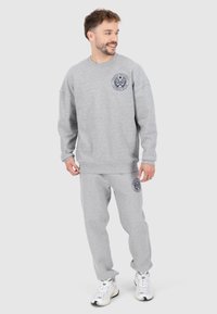 Set di felpa e pantaloni tuta grigi, con un logo rotondo sul petto e sulla coscia, realizzato in materiale morbido con polsini a coste sulle maniche e sull'orlo.