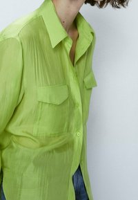 Translucent lime green button-up shirt with two chest pockets, a pointed collar, and a slightly loose fit. Soft texture and light fabric.