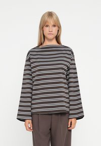 Top a maniche lunghe a righe marroni con linee azzurre, featuring un collo a barca e una vestibilità rilassata. Abbinato a pantaloni scuri a vita alta.