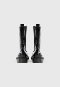 Bottines en cuir noir avec une finition brillante, fermeture éclair sur le côté, bout arrondi et talon épais. Texture lisse et design épuré.