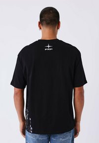 Camiseta de algodón negra con un logo blanco "PXP" en la parte posterior. Manga corta y un corte relajado, que muestra un diseño texturizado en el dobladillo.