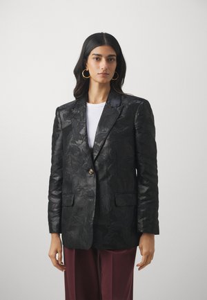 Svart blazer med blomstermønster, enkel knappelukking, slagkrage og to frontlommer. Brukt over en hvit topp og burgunderbukser.