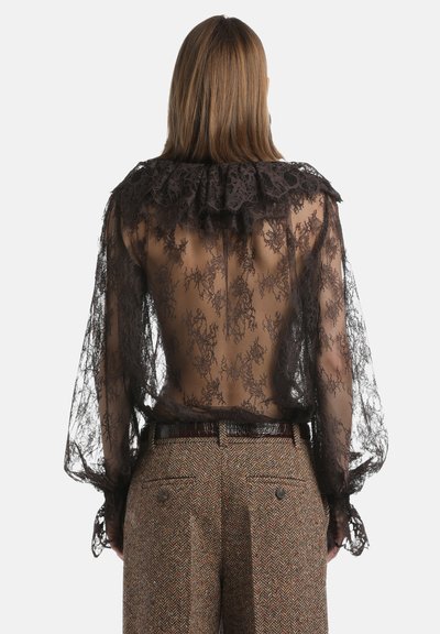 Zwarte kanten blouse met gerimpelde kraag, doorschijnende stof, lange mouwen en ingewikkelde bloemenpatronen, gecombineerd met bruine visgraatbroek.