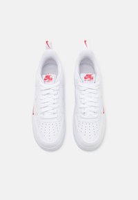 Sneakers in pelle bianca con accenti rossi. Le caratteristiche includono punte perforate, sistema di allacciatura, collo imbottito e linguetta e tallone con marchio.