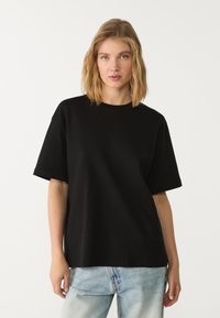 Sort oversized t-shirt i bomuldsstof, kortærmet, rund hals, parret med lyseblå denim jeans. Glat tekstur, afslappet pasform.