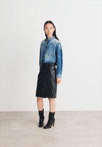 Camicia di jeans con una finitura blu sbiadita, abbinata a una gonna a matita in pelle nera e stivaletti neri con tacco alto. Design semplice e strutturato.