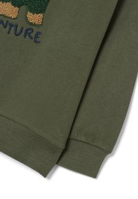 Sweatshirt vert olive en mélange de coton, avec des poignets côtelés et un design brodé représentant un ours texturé et le texte "AVENTURE".