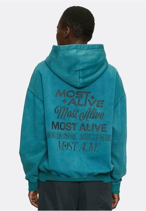 Türkise übergroße Hoodie mit unterschiedlichen Textgrafiken in Schwarz, mit einem Pulloverdesign und einer geräumigen Kapuze. Weicher, strukturierter Stoff.