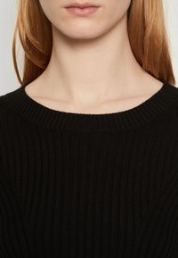 Maglione nero a costine con colletto rotondo, caratterizzato da una texture orizzontale e un materiale morbido, tagliato a close-fitting nella zona del collo.