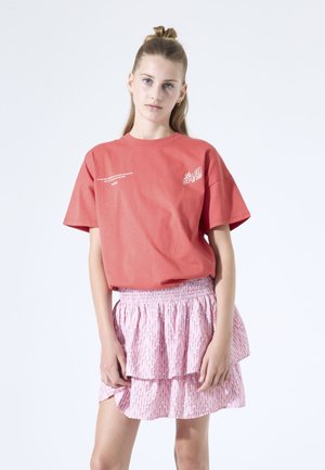 Korallfarbenes Baumwoll-T-Shirt mit kurzen Ärmeln und weißem Grafikttext. Kombiniert mit einem pinkfarbenen gestuften Rock mit geometrischem Muster und elastischem Bund.