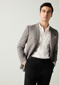 Grau wollener Blazer mit slim fit, cremefarbenem Hemd, schwarze Hose und einem Taschentuch mit floralem Muster.