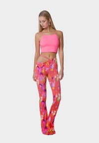 Top corto a coste rosa abbinato a pantaloni a campana con stampa floreale dai colori vivaci di rosa, viola e verde.
