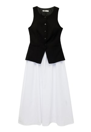 Veste noire sans manches à boutons portée sur une longue jupe blanche évasée, les deux posées à plat sur un fond blanc.