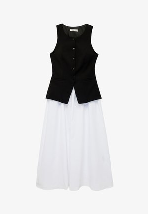 Veste noire sans manches à boutons portée sur une longue jupe blanche évasée, les deux posées à plat sur un fond blanc.