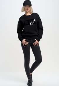 Černá mikina s lesklým potiskem "BIG STAR", spárovaná s černými slim-fit džíny a černými teniskami. Jednoduchý, neformální design.