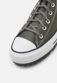 Zöld bőr sneakers fehér gumi orral és fekete talppal. Szürke fűzőkkel és kontrasztos fehér varratokkal rendelkezik.