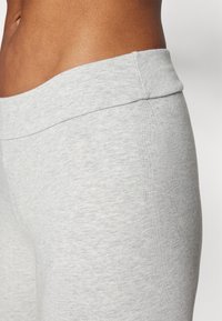 Tissu extensible gris avec une texture douce et lisse. Ceinture large qui repose à plat sur la peau. Design ajusté adapté aux activités sportives.