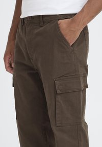 Brown cargo pants made of cotton with a straight cut. Features side pockets and a button closure, exhibiting a durable texture.