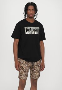 Zwarte T-shirt met metallic "justcavalli" logo, gecombineerd met beige shorts met luipaardprint en een trekkoord in de taille.