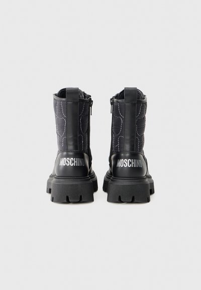 Botas de tobillo acolchadas negras con suelas gruesas y acentos de goma. Presentan un logo en el talón, cremalleras laterales y un acabado texturizado.