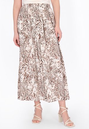 Nő hosszú, légies, állatmintás szoknyában, bézs, pántos magassarkú szandállal egy egyszínű fehér háttér előtt.