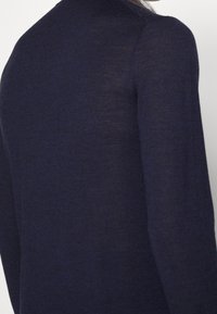 Námořnická modrá lehká pletená svetr s texturovaným povrchem, s vysokým výstřihem a dlouhými rukávy, který předvádí jednoduchý a elegantní siluetu.