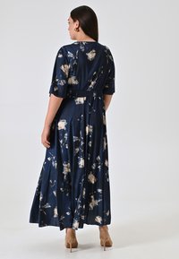 Marineblaues Blumen-Maxikleid mit kurzen Ärmeln, gerafftem Taillendetail und schwingendem Rock. Es zeichnet sich durch eine weiche satinartige Textur und beigen Floralakzenten aus.
