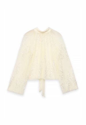 Cape blanc cassé à texture plissée, parsemée de sequins. Comprend un col montant et des liens à la taille.